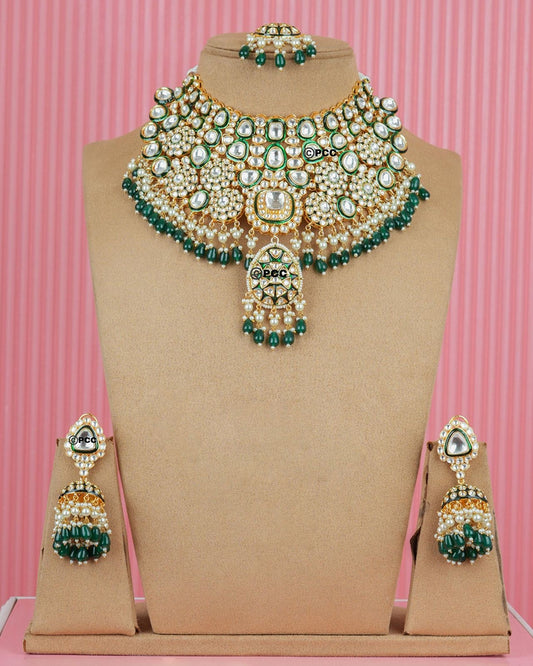 A mannequin showcasing a Royal Bridal Queen Necklace Set with gold tone, green accents, and sparkling embellishments.