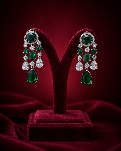 A pair of dramatic drop earrings with large oval green emerald-cut stones, smaller round green and clear stones, and teardrop-shaped green drops 