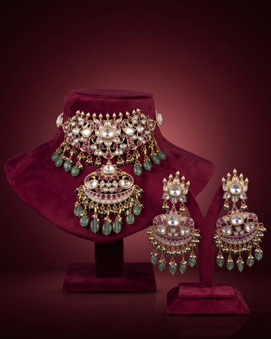 Luxury Kundan and Polki bridal choker necklace set featuring intricate ruby-red stones, green beads, pearl detailing, matching statement earrings, and a traditional Indian bridal jewellery design.