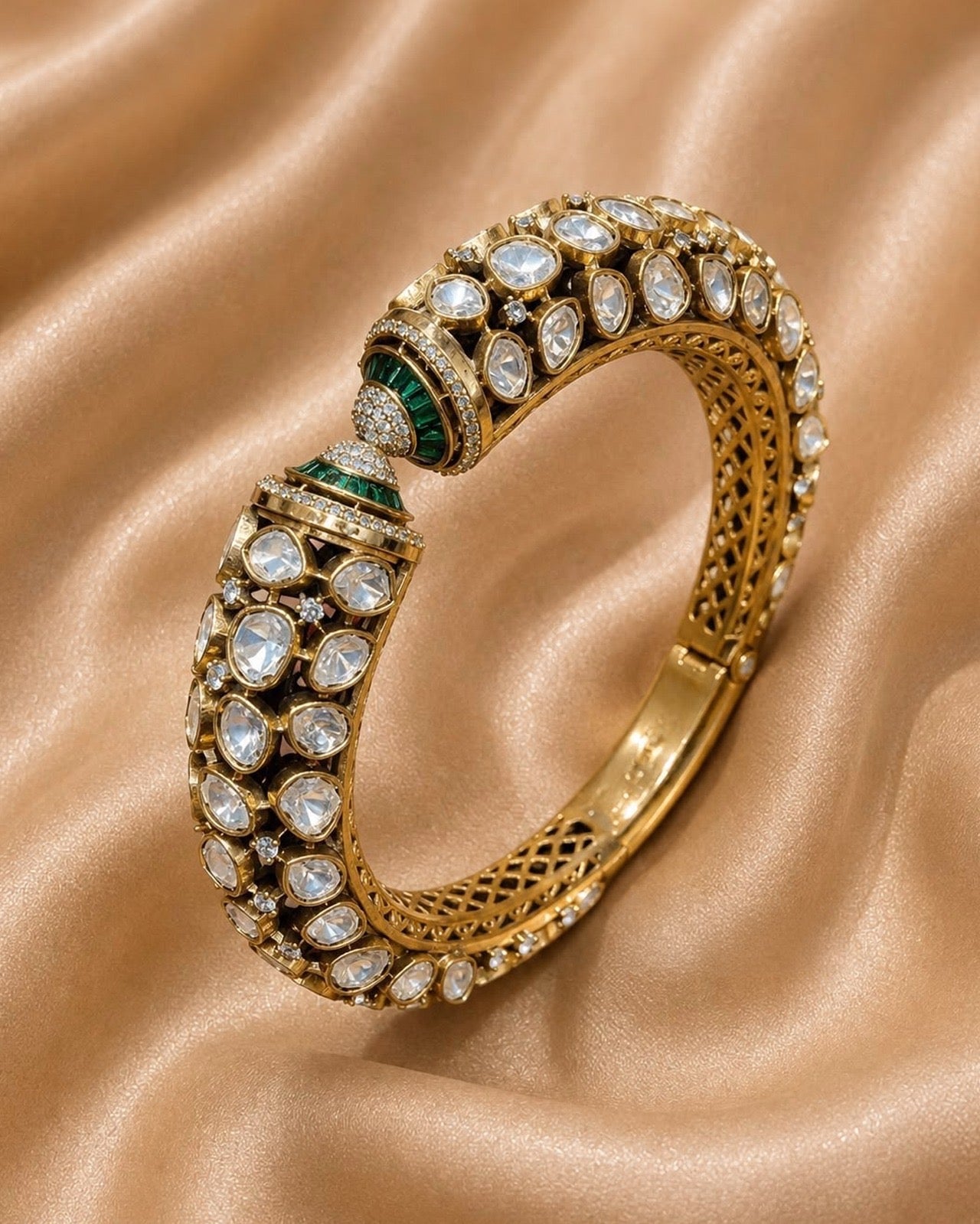 An ornate gold bangle bracelet adorned with clear stones and green emerald accents 