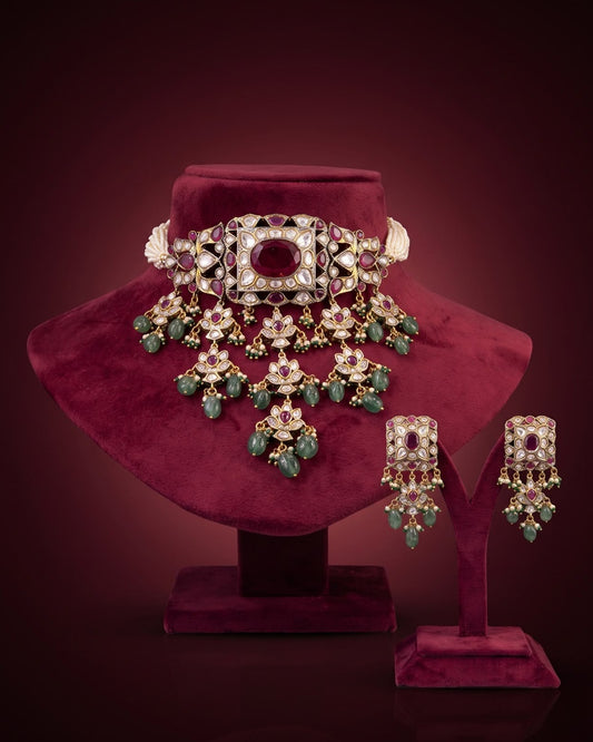 Elegant Kundan and Polki bridal choker necklace set with ruby-red stones, green beads, intricate gold detailing, matching statement earrings, and a luxurious traditional Indian design.