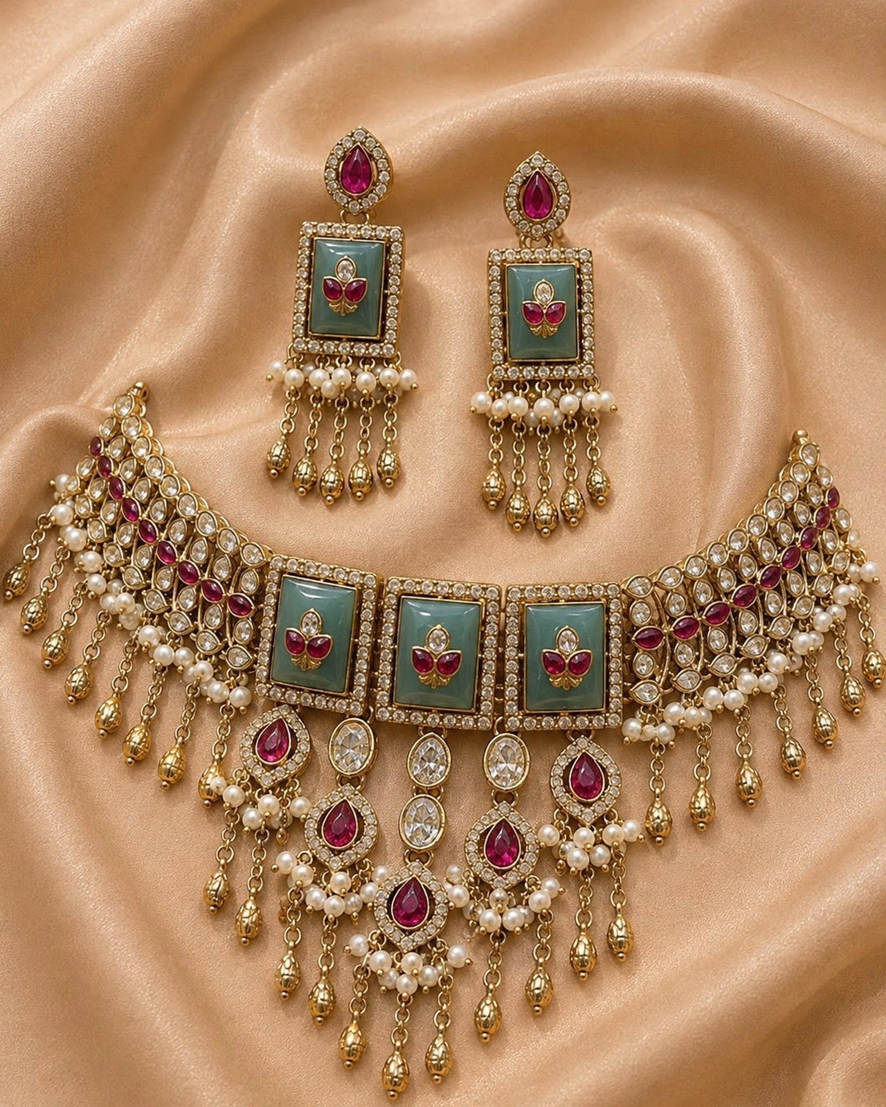 An ornate gold-toned jewelry set featuring a choker necklace and matching earrings, decorated with turquoise green enamel panels, red stones, and white pearl-like beads, displayed on a beige satin fabric background.