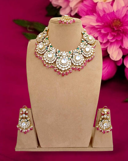A Pink Polki Necklace Set displayed on a mannequin against a pink background with flowers. The set includes a necklace and earrings with pink and white stones.